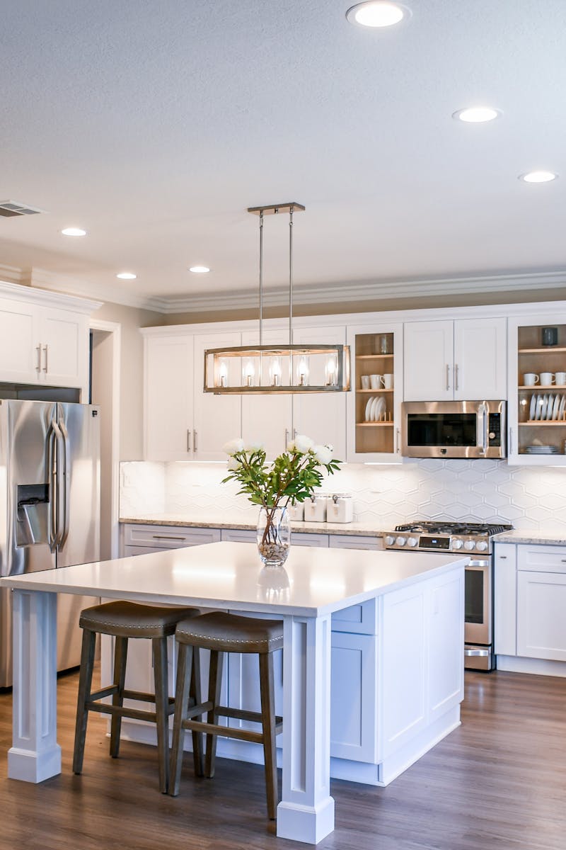 Elegant white kitchen featuring an island, modern appliances, and ample natural light.