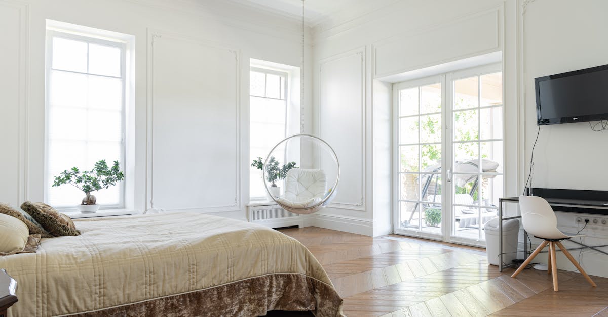 Spacious modern bedroom with wooden floors, elegant decor, and abundant natural light from large windows.